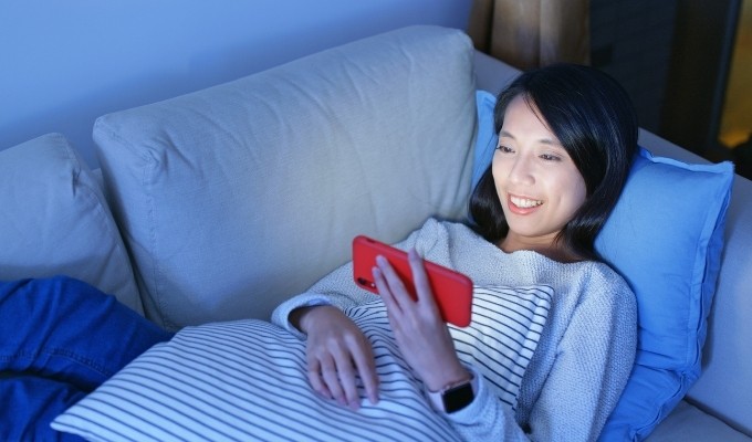 Woman watching movie on phone while laying on couch smiling