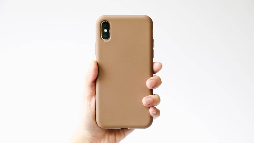 A hand holding a smartphone with a brown case